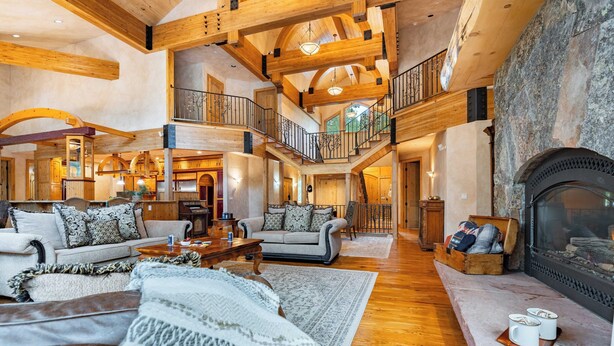 A spacious living area with a fireplace, wooden beams, and a high ceiling.