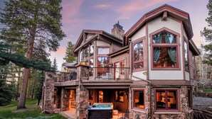 A large, multi-story house with a stone exterior, a hot tub, and a patio with outdoor seating.
