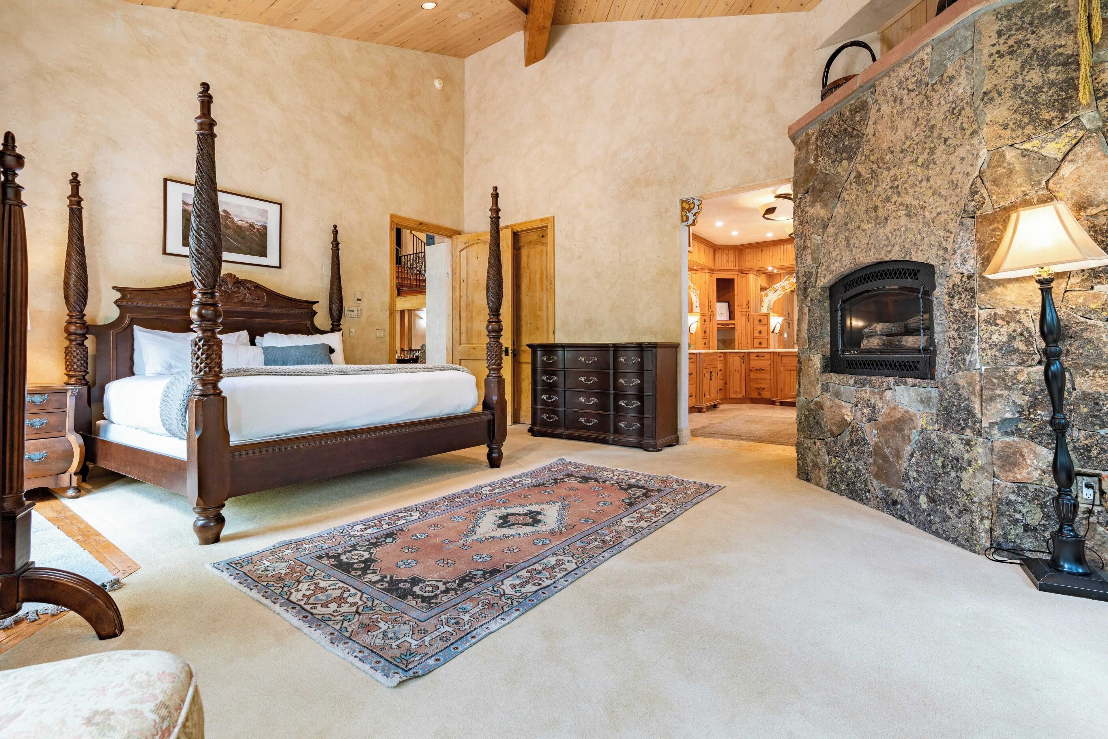 Un dormitorio con cama con dosel, chimenea de piedra y un tapete grande.