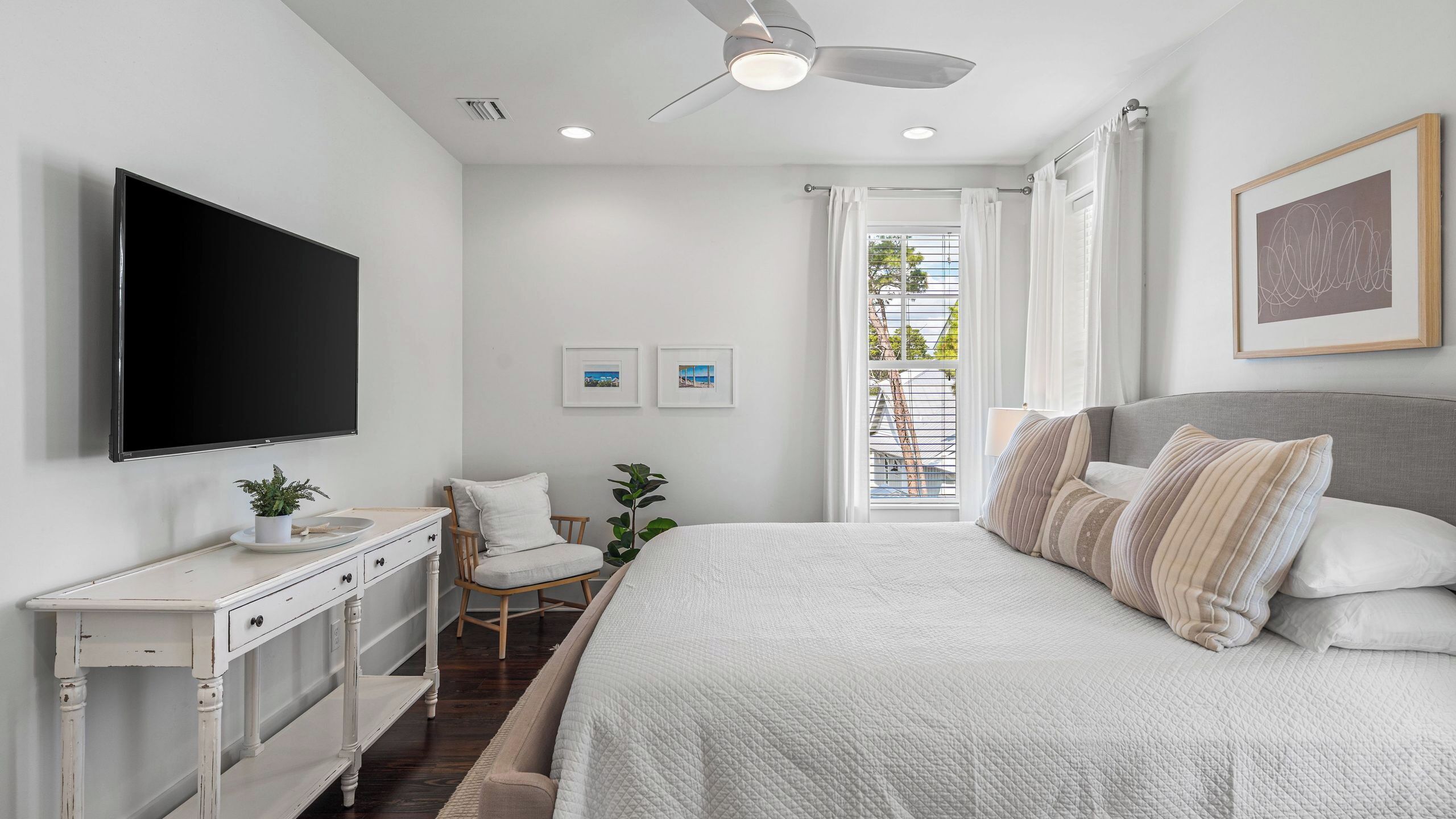 Un dormitorio con cama, televisor, cómoda, silla y ventana con vistas.