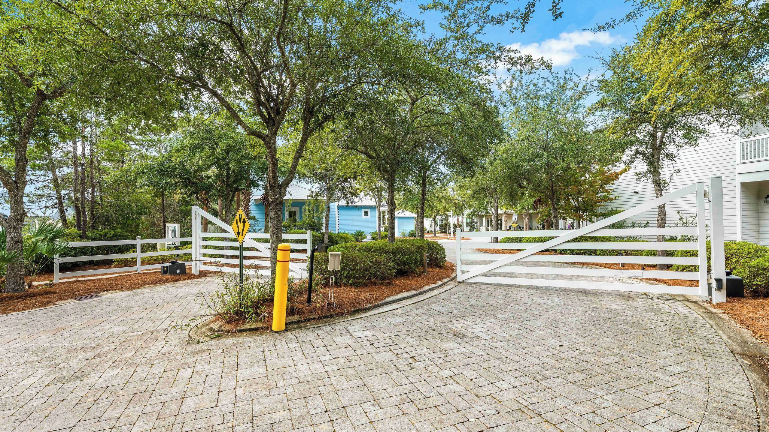 A paved driveway leading to a gated entrance with a white fence and a yellow bollard.