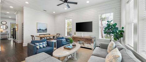 A spacious living room with a ceiling fan, a TV, and a dining area with a wooden table and chairs.
