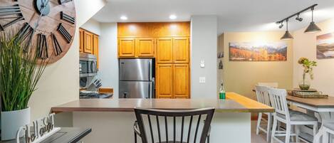 Una cocina moderna con armarios de madera, un refrigerador de acero inoxidable y un comedor con sillas blancas y una mesa.