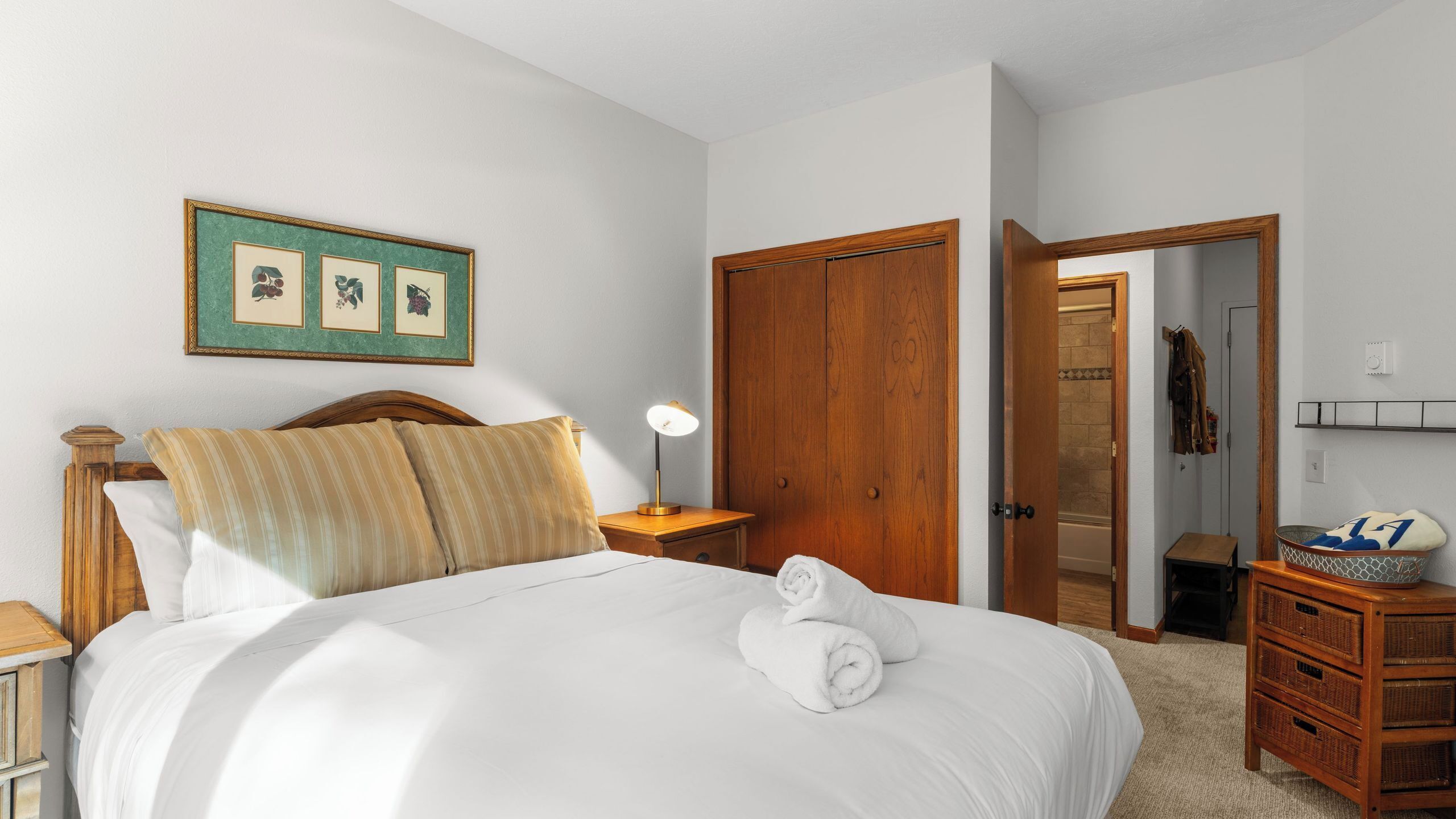 A neatly made bed with a wooden headboard, a bedside lamp, and a framed picture above it.
