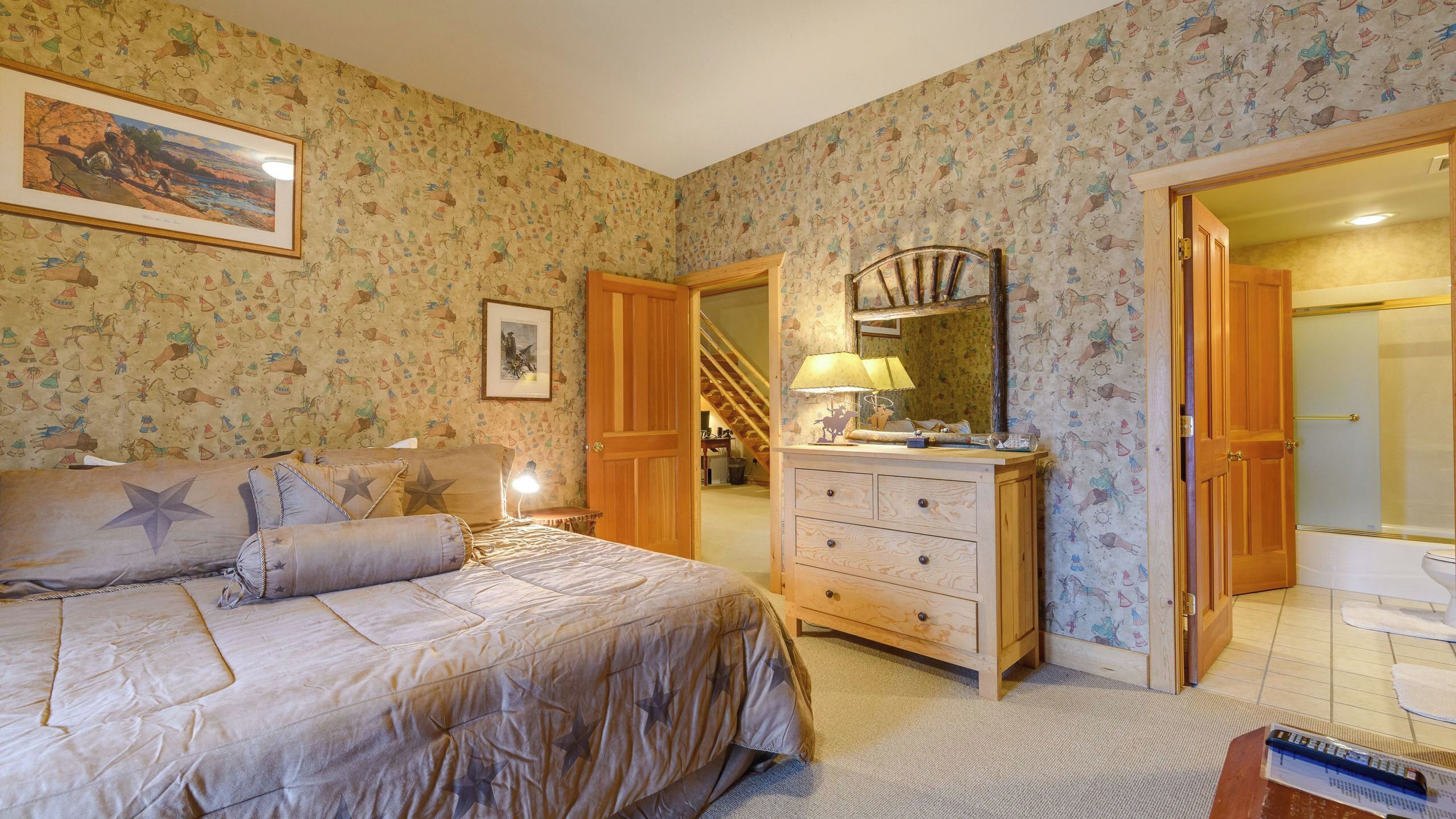A bedroom with a bed, dresser, mirror, and a door leading to another room.