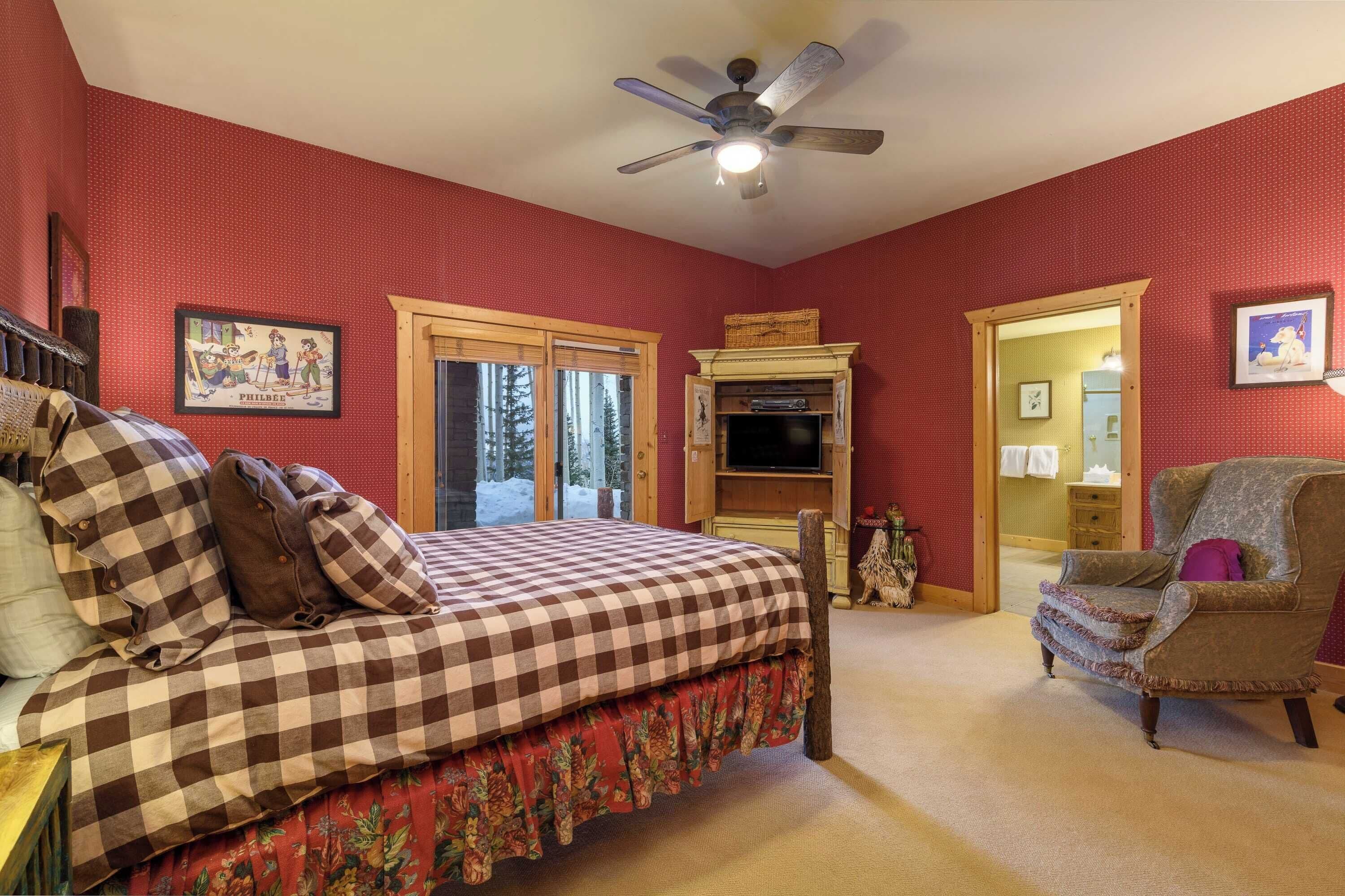 A bedroom with a checkered bedspread, a wooden chair, and a ceiling fan.