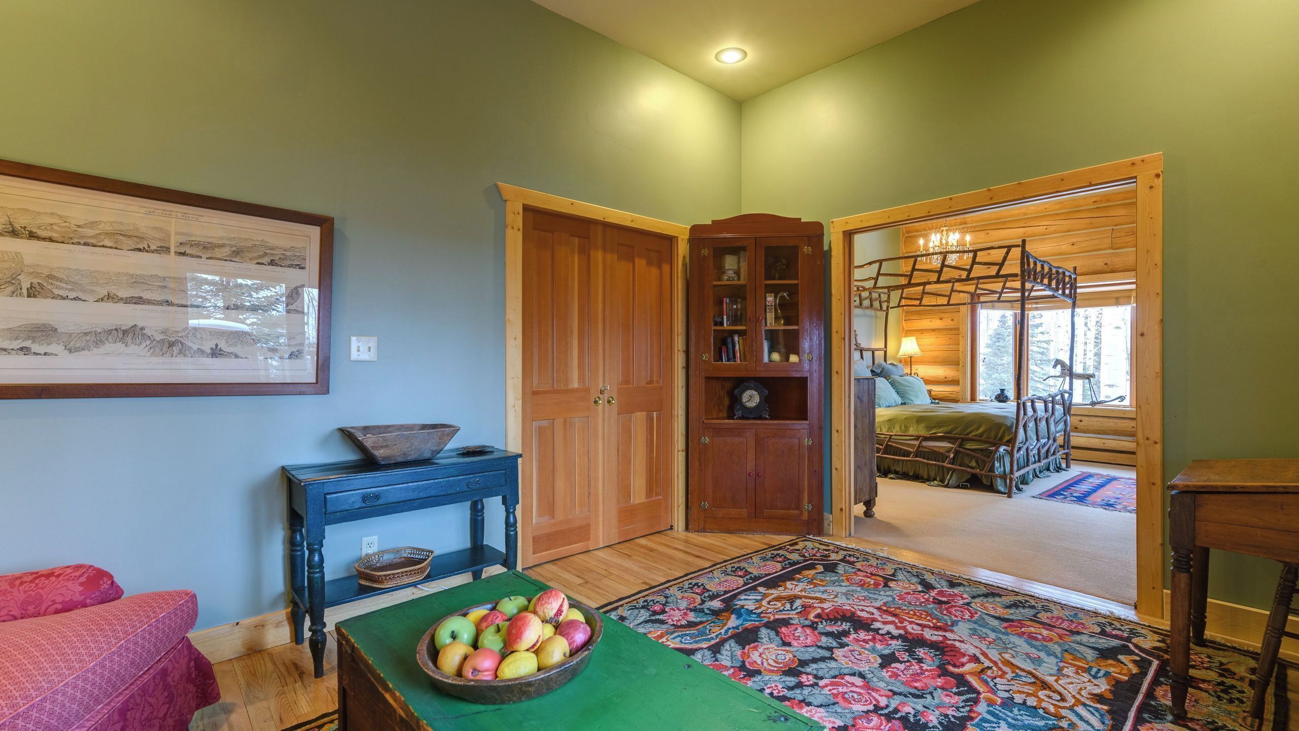 A room with a wooden bed, a wooden cabinet, a framed picture on the wall, and a bowl of fruit on a table.