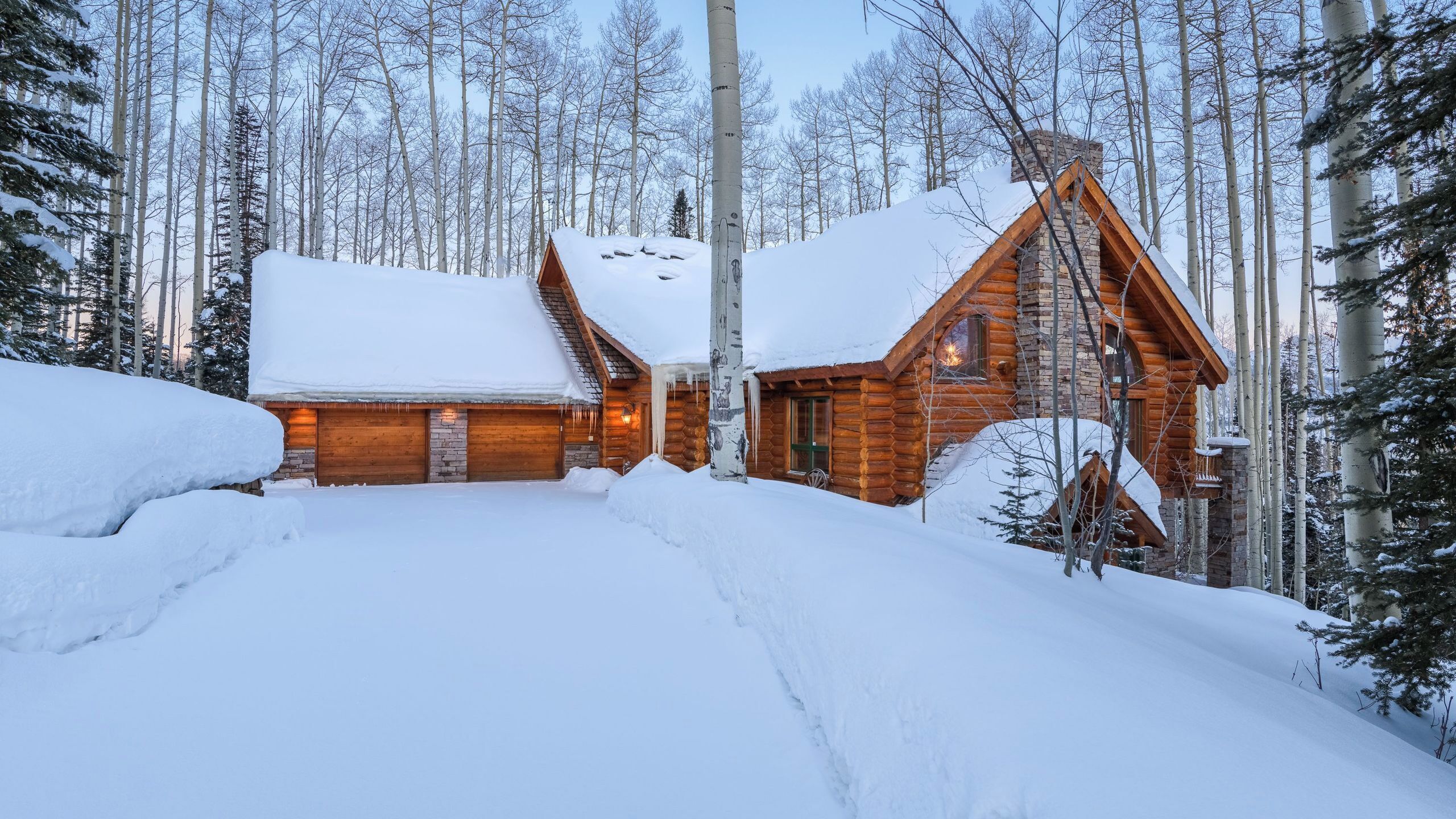 A log cabin with a snow-covered roof, surrounded by a forest.