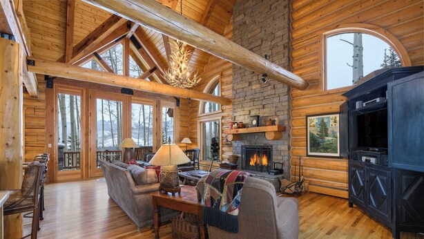 A log cabin interior with a fireplace, wooden furniture, and large windows. - Snowdrift Cabin by Avantstay Breathtaking Home w/ Prime Ski Access (Telluride)