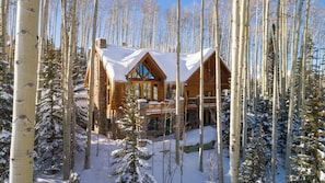 Une cabane en rondins dotée d’un balcon, entourée d’arbres couverts de neige.