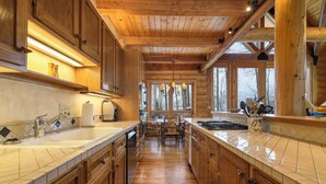 A wooden cabin interior with a kitchen featuring a large island, wooden cabinets, and a dining area with a table and chairs. - Snowdrift Cabin by Avantstay Breathtaking Home w/ Prime Ski Access (Telluride)