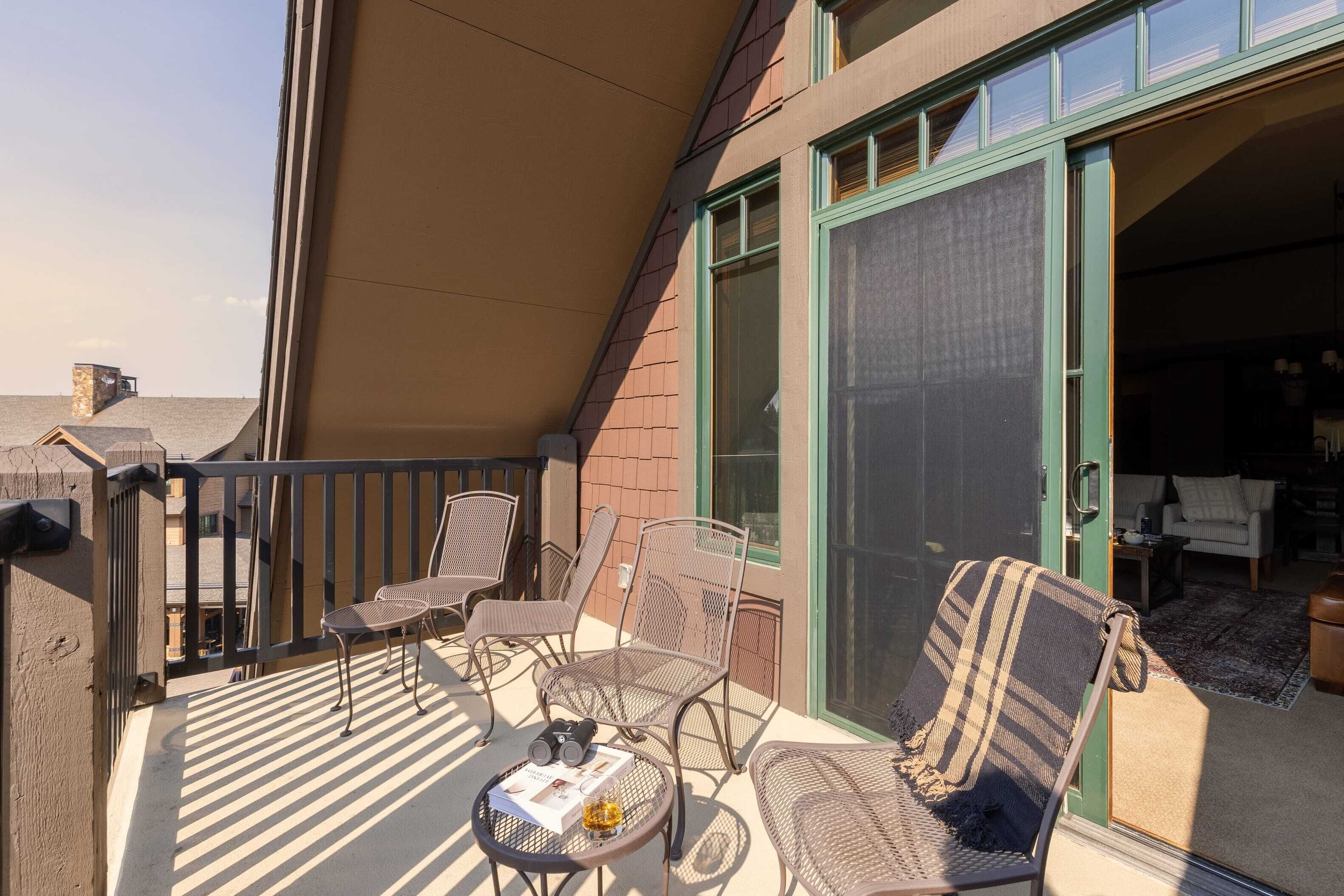 Un balcon avec des sièges d’extérieur, une table avec un magazine et une bouteille, et une vue sur l’intérieur à travers une porte vitrée.