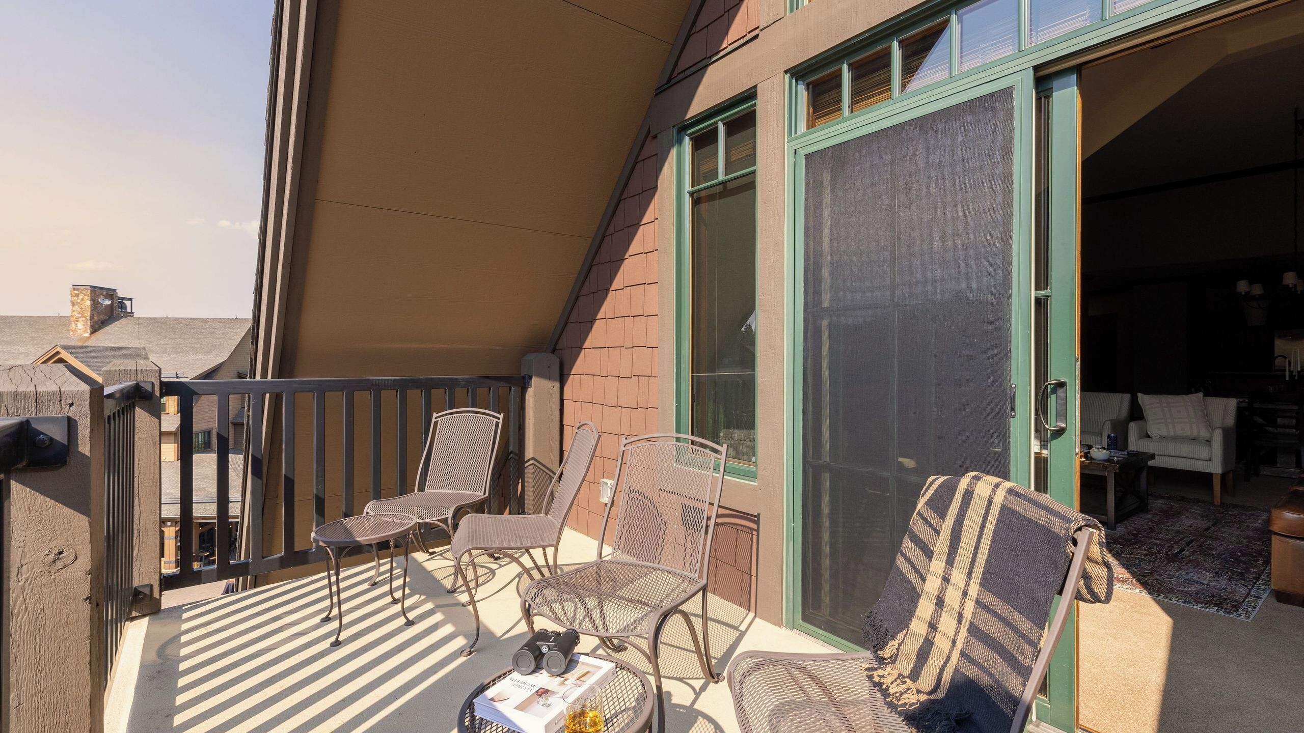 A balcony with wicker chairs, a table with a book and binoculars, and a sliding glass door leading to an interior space.