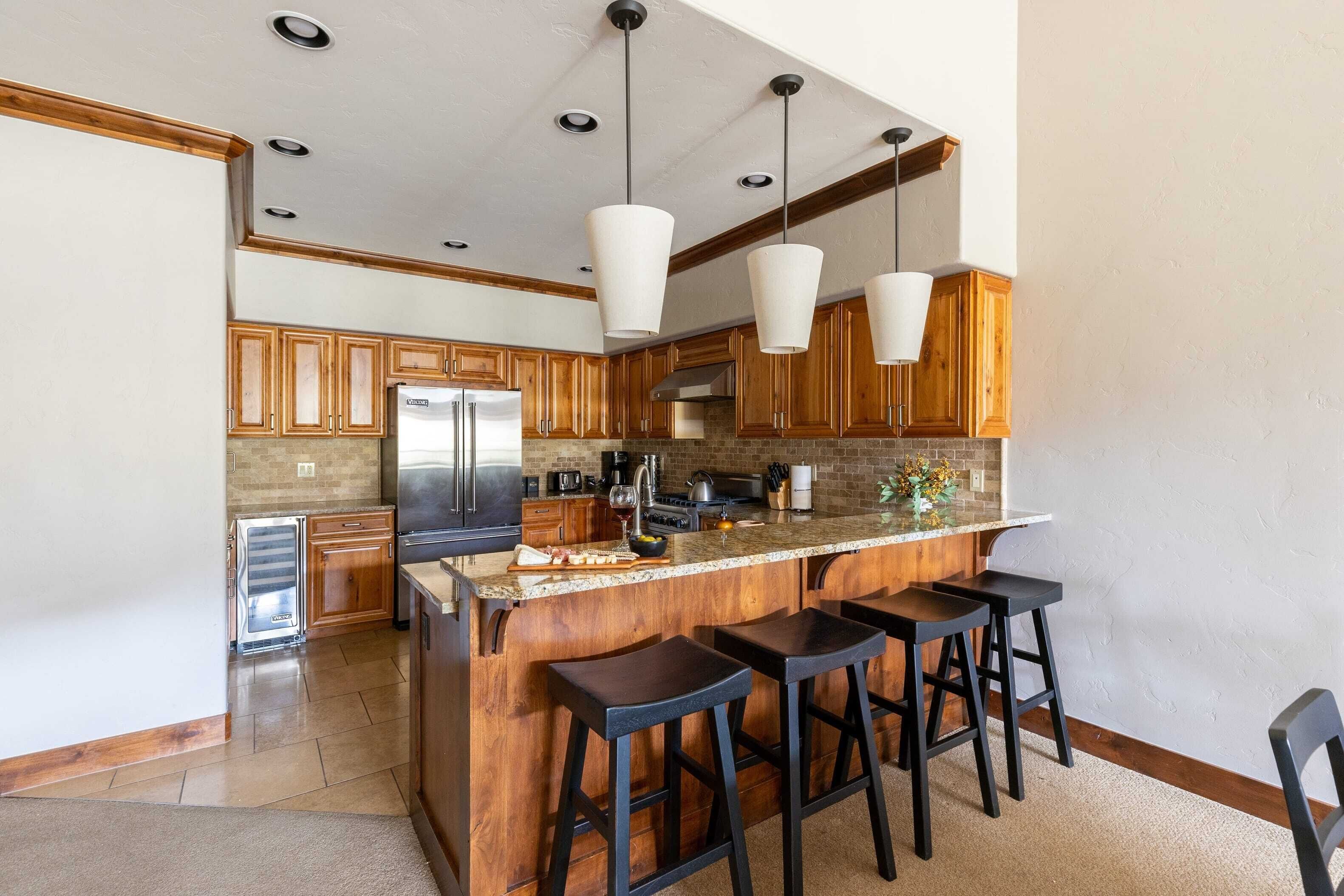 A modern kitchen with wooden cabinets, a central island with bar stools, stainless steel appliances, and pendant lighting.