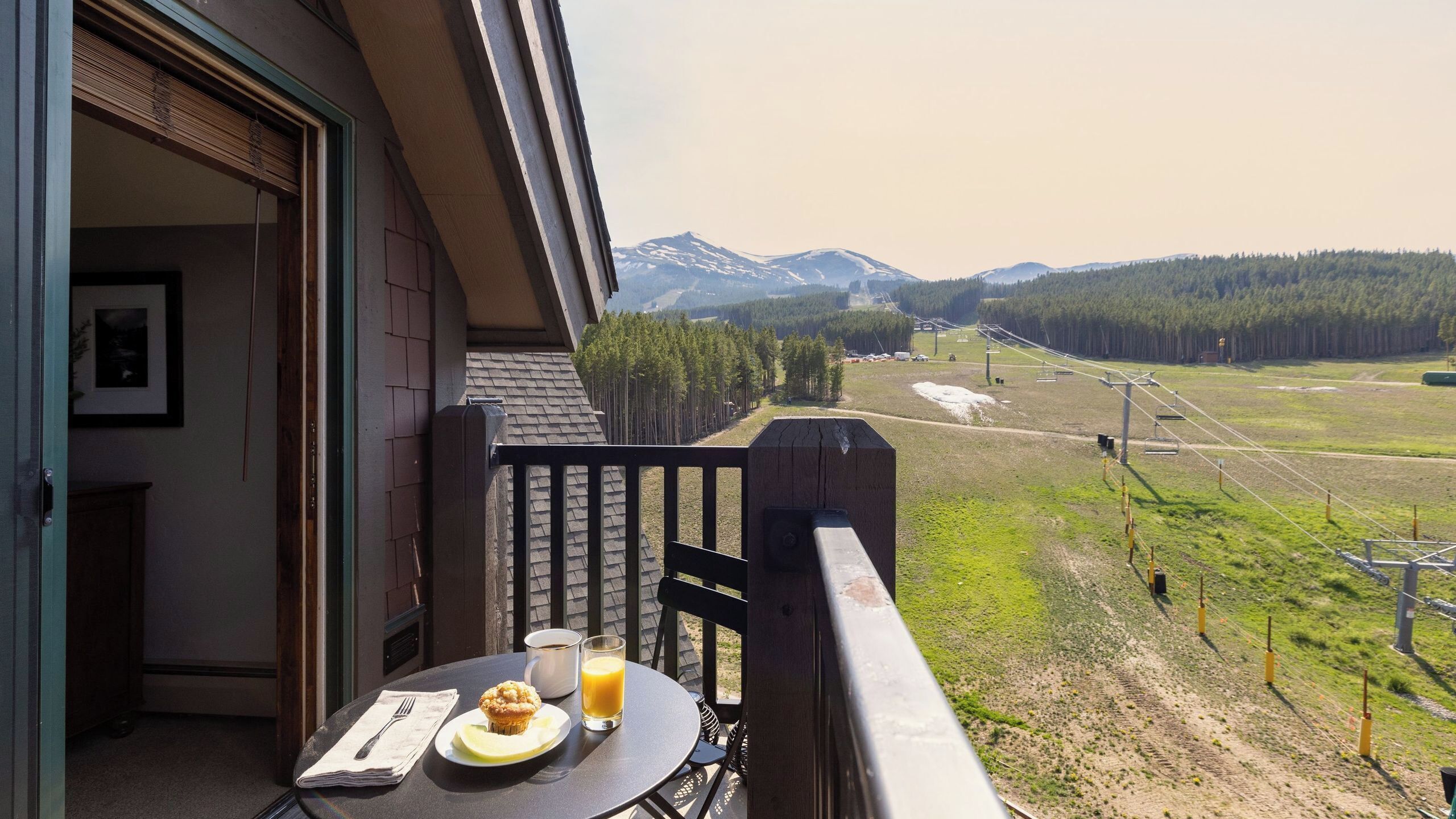 A balcony with a table, a muffin, a glass of orange juice, and a framed picture on the wall.