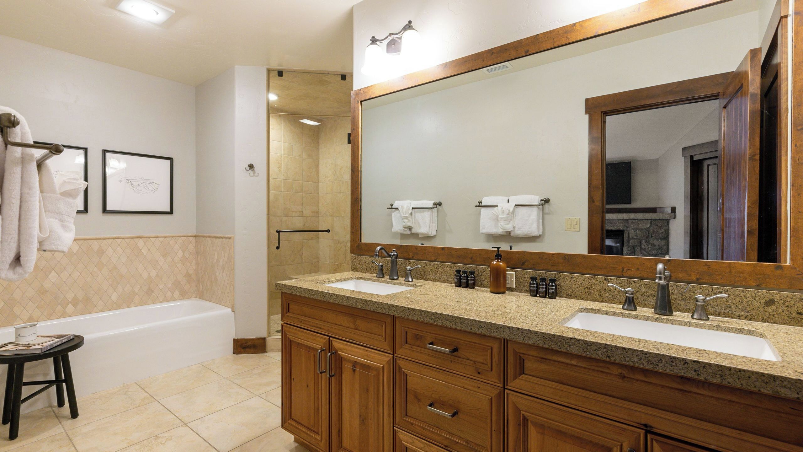 A bathroom with a bathtub, two sinks, wooden cabinets, a large mirror, and a towel rack.