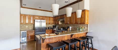Une cuisine moderne avec des meubles en bois, un réfrigérateur en acier inoxydable, un plan de travail en granit et des luminaires suspendus.