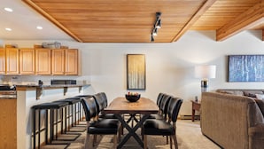 Een moderne keuken met houten kastjes, een centraal eiland en een eethoek met een houten tafel en zwarte stoelen.