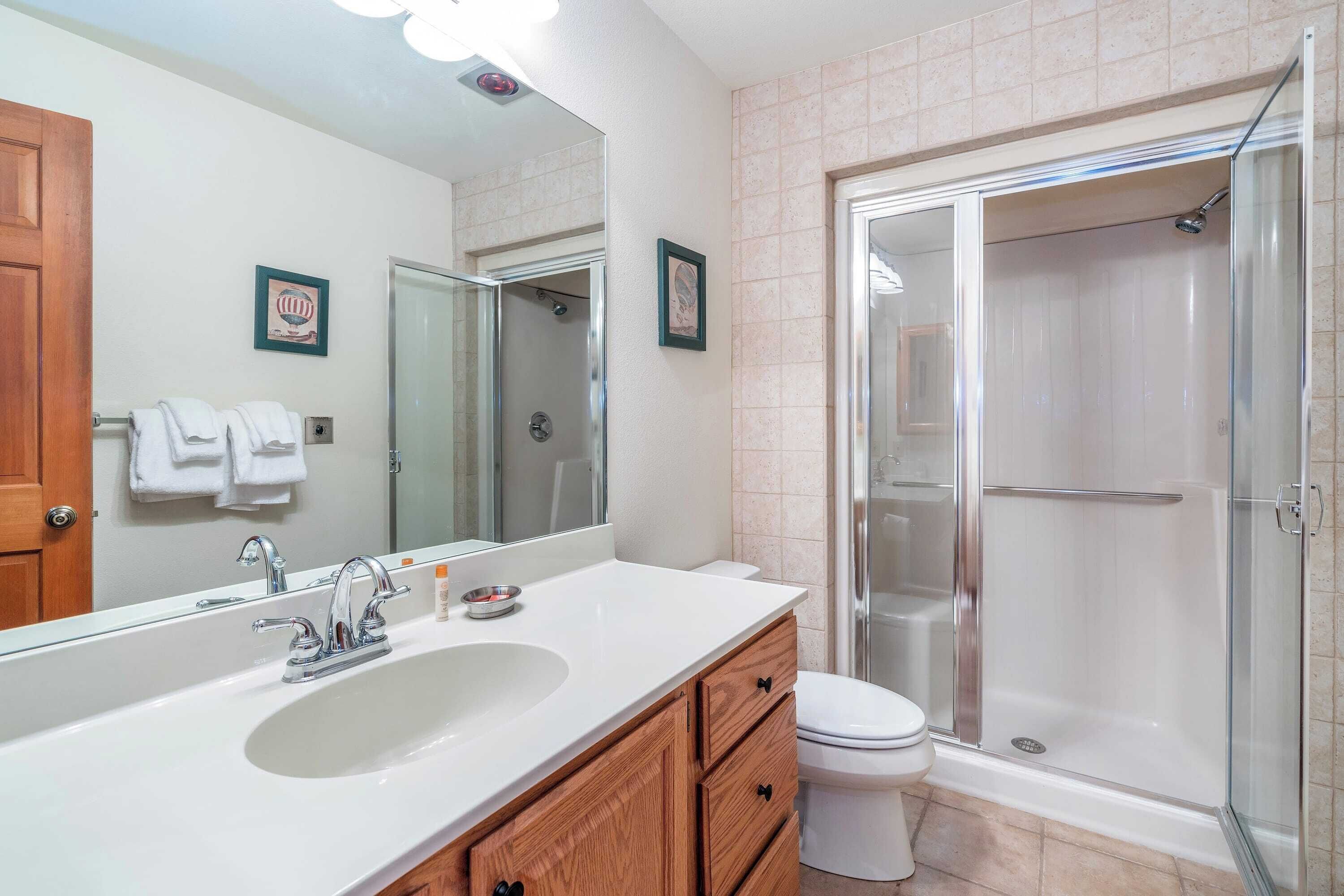 A bathroom with a large mirror, a sink, a toilet, and a walk-in shower.