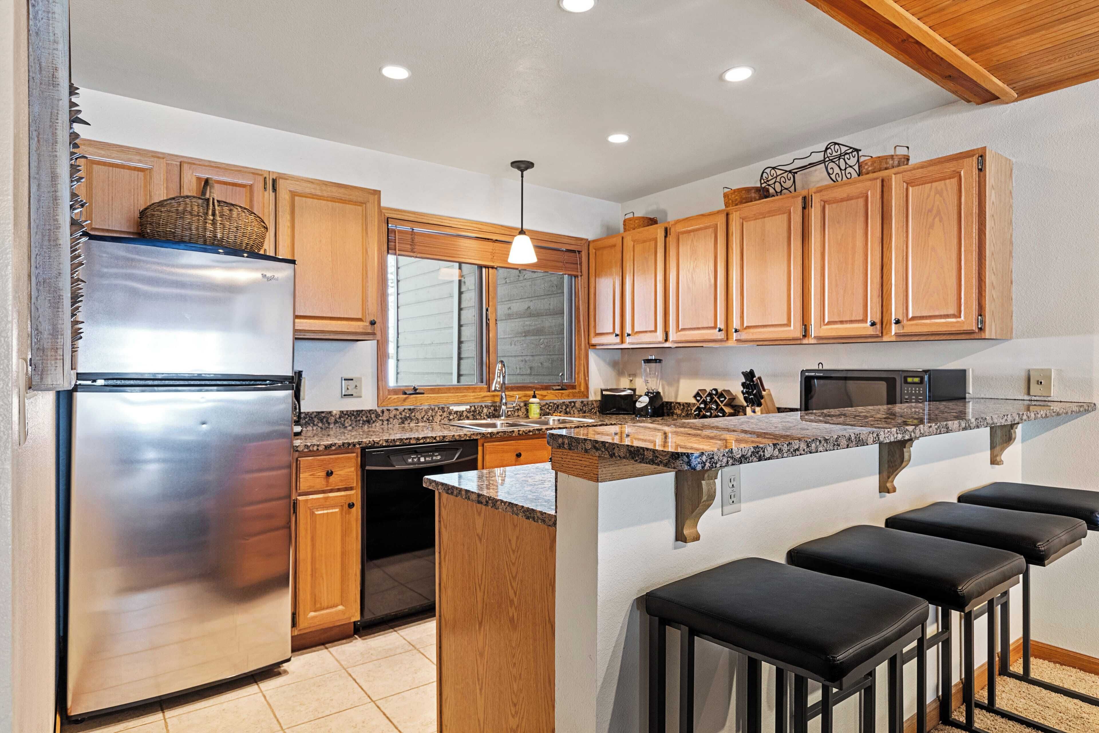 A kitchen with wooden cabinets, a stainless steel refrigerator, a granite countertop, and a built-in island with bar stools.