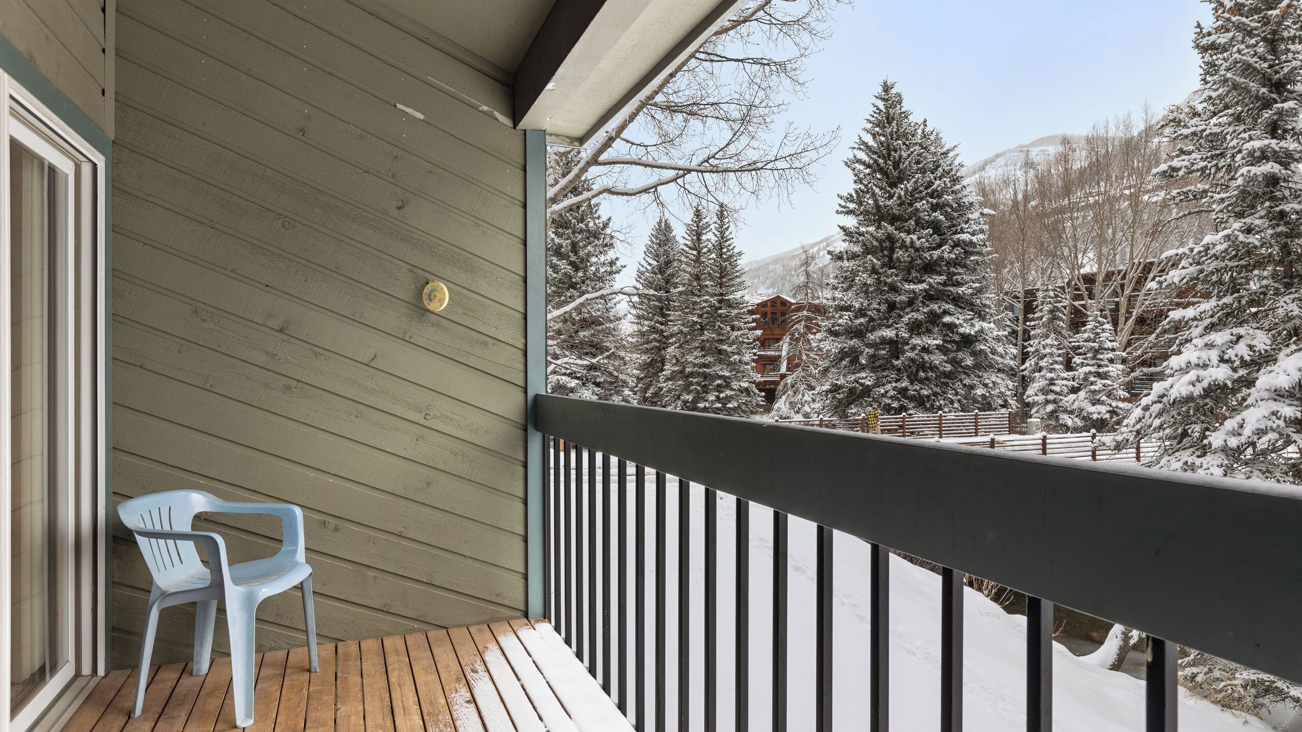 Un balcon en bois offrant une vue sur des arbres et des montagnes enneigés.