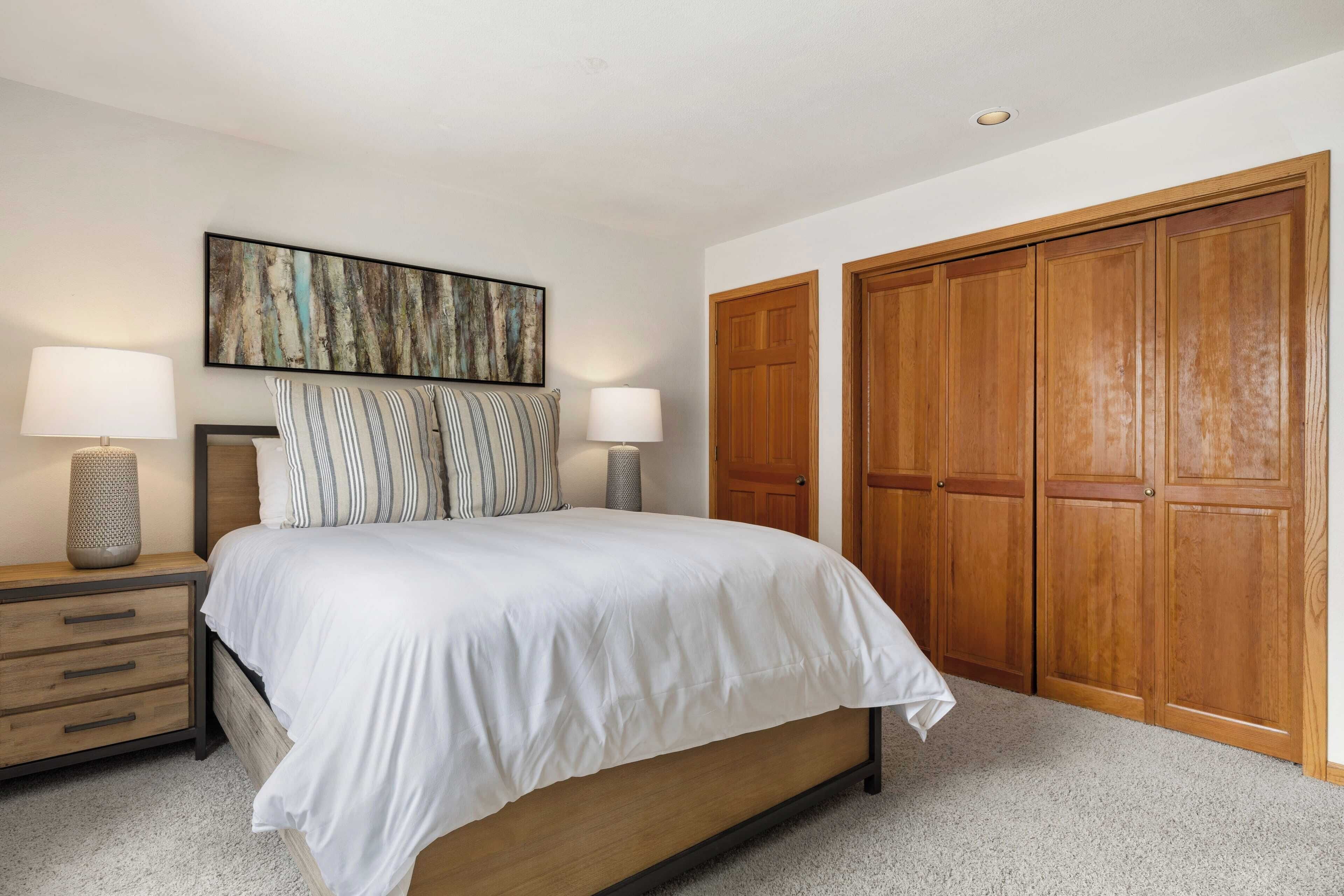 A bedroom with a large bed, wooden wardrobe, and a painting on the wall.
