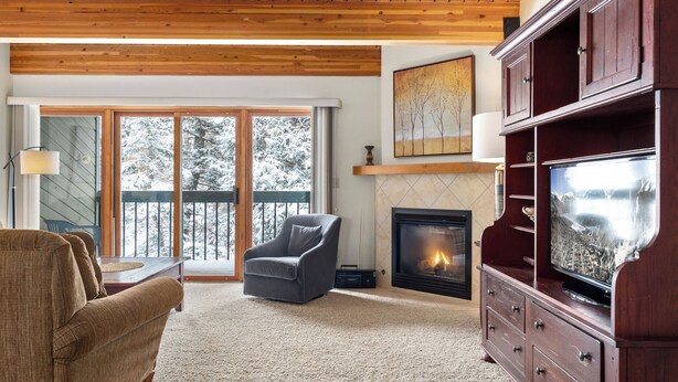 Een gezellige woonkamer met een open haard, een groot raam met uitzicht op met sneeuw bedekte bomen en een televisie op een houten kast.