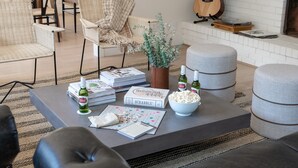 A cozy living room with a coffee table, books, a bowl of popcorn, and a guitar against a white brick wall.