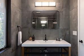 A modern bathroom with a large mirror, white sink, and a towel hanging on the wall.