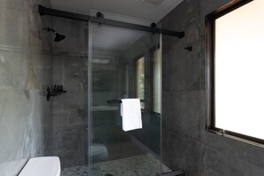 A modern bathroom with a glass shower enclosure, a white toilet, and a large window providing natural light. - Mataro by Avantstay Large & Elegant Home in Santa Rosa w/ Hot Tub & Games (Santa Rosa)