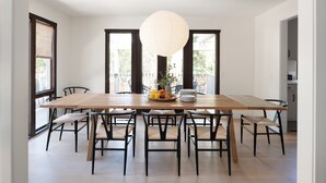 A dining area with a large wooden table, black chairs, and a hanging light fixture.