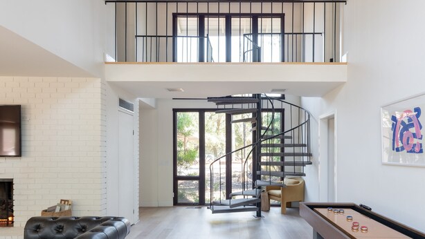 A spacious living area with a fireplace, a pool table, and a spiral staircase leading to an upper level.