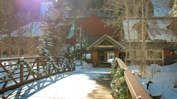 A lodge entrance with a wooden walkway, snow-covered trees, and a Christmas wreath. - Cimarron Lodge 20 by Avantstay Ski In/ Ski Out Condo in Ideally Located Complex w/ Hot Tubs! (Telluride)