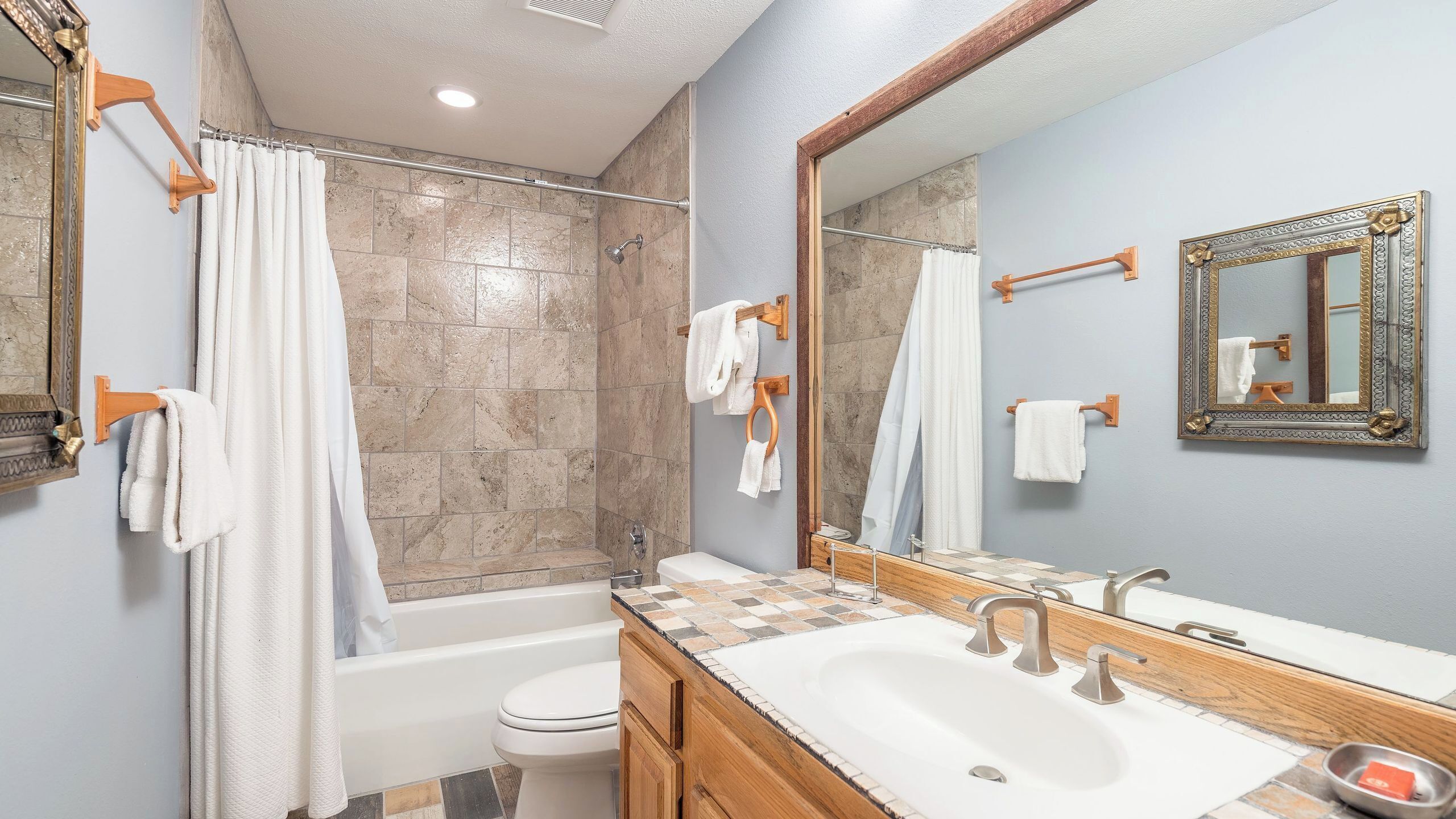 Un bagno con vasca, WC e lavabo, asciugamani appesi a ganci e uno specchio sopra il lavabo.