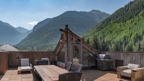 A wooden deck with a table and chairs, a grill, and a view of mountains. - Ghostriders 11 by Avantstay Top Floor Condo w/ Large Patio & Mountain Views! (Telluride)