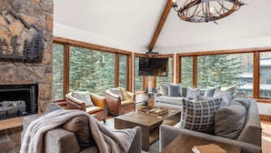 A cozy living room with stone walls, large windows, a fireplace, leather armchairs, and a television. - Ghostriders 11 by Avantstay Top Floor Condo w/ Large Patio & Mountain Views! (Telluride)