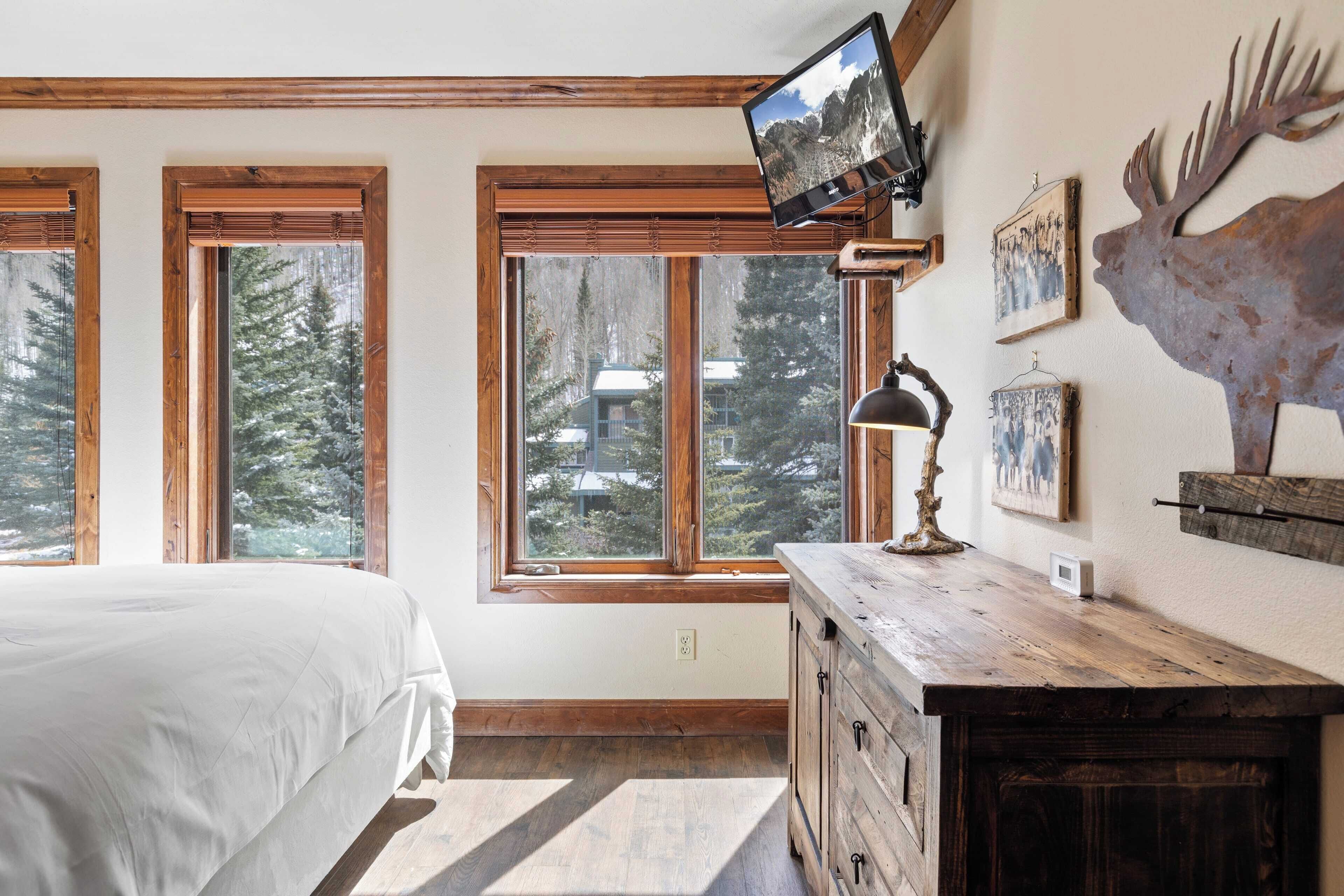Une chambre à coucher avec un lit, une commode en bois, un téléviseur fixé au mur et une décoration représentant une tête de cerf.