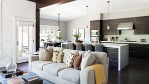 A modern living room with a sofa, a coffee table with books and a vase, and a kitchen with dark cabinetry and a large island. - Quartz by Avantstay Stunning Home In Truckee w/ Views (Truckee)