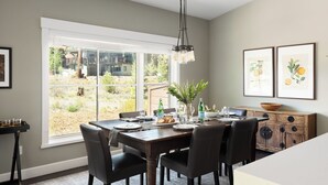 A dining area with a large window, a wooden dining table, black chairs, a chandelier, and framed artwork on the wall. - Quartz by Avantstay Stunning Home In Truckee w/ Views (Truckee)