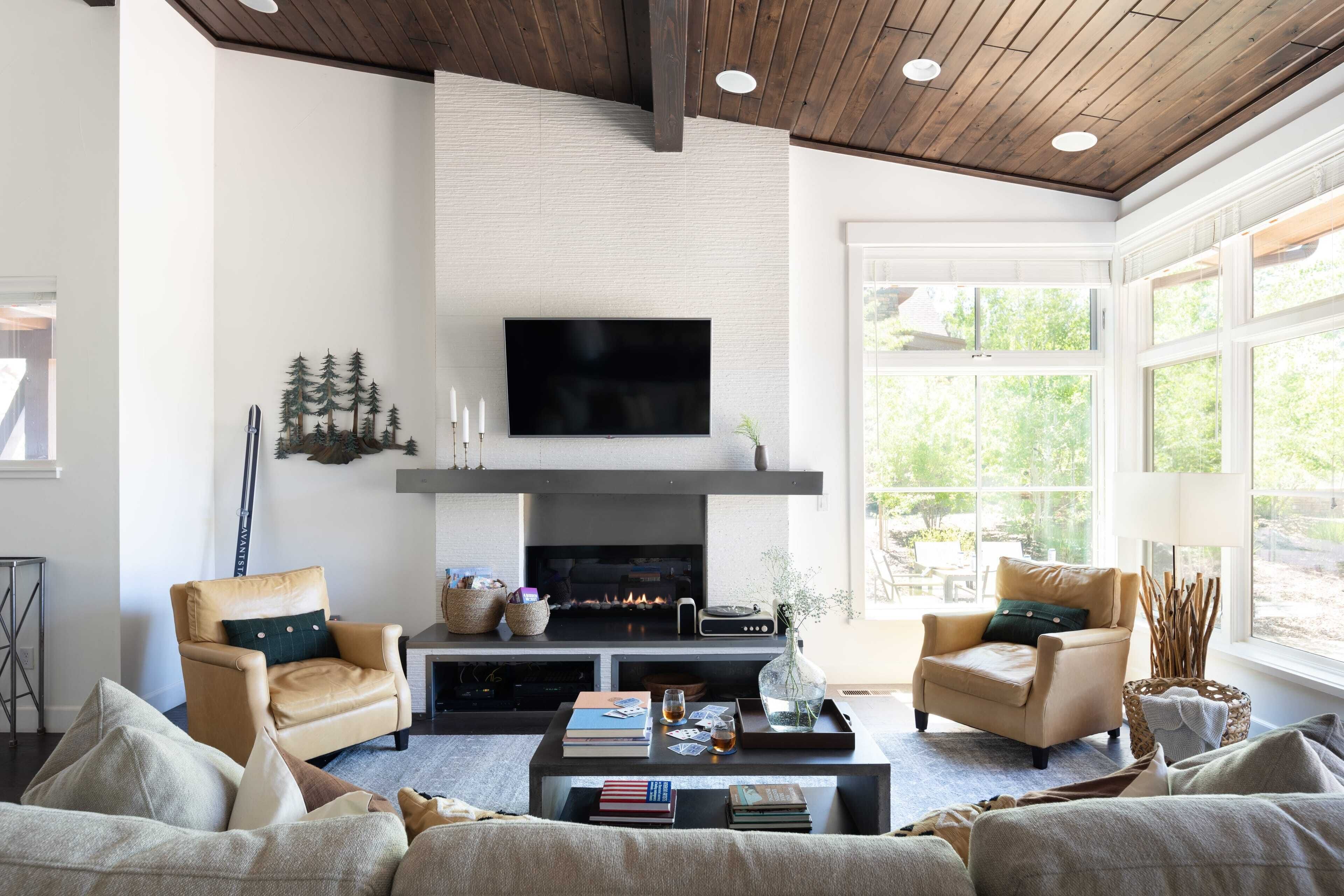 Una sala de estar moderna con chimenea, sillones de cuero, una mesa de centro con libros y vasos, y ventanas amplias.
