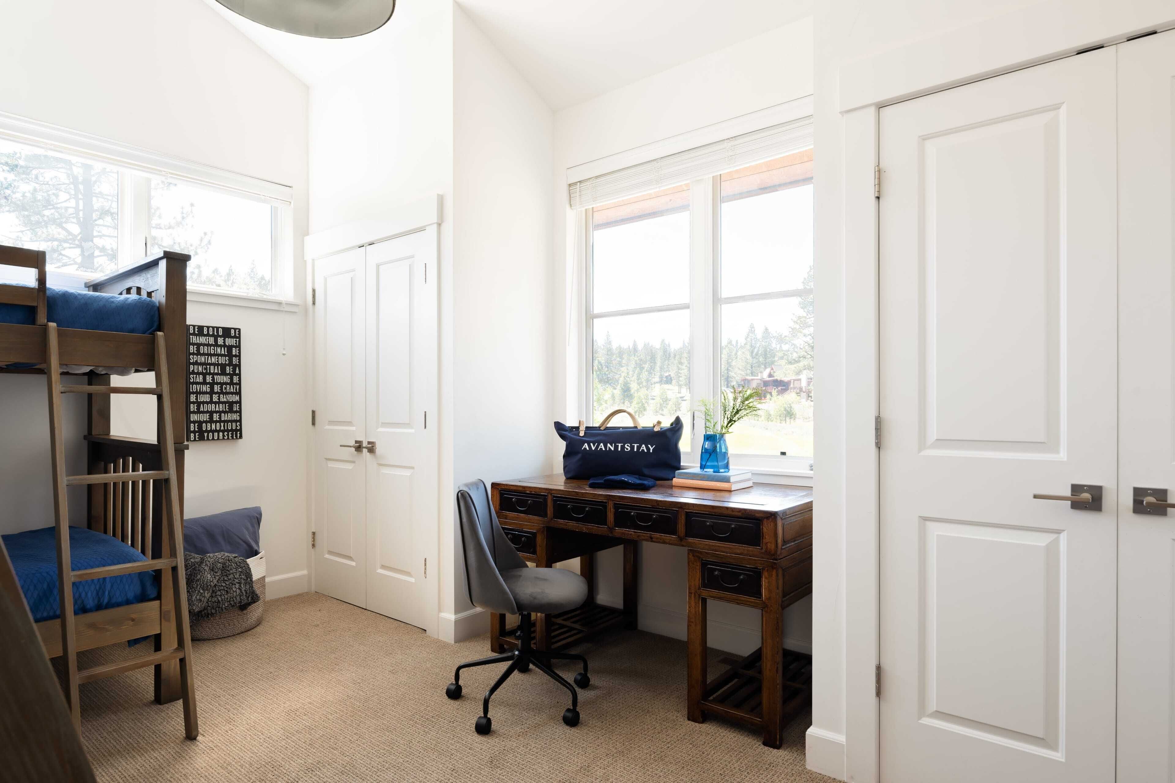 A bedroom with a bunk bed, desk, chair, and a window with a view of trees.