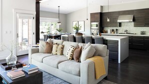 A modern kitchen with dark wood cabinets, a central island, and a dining area with a table and chairs. - Quartz by Avantstay Stunning Home In Truckee w/ Views (Truckee)