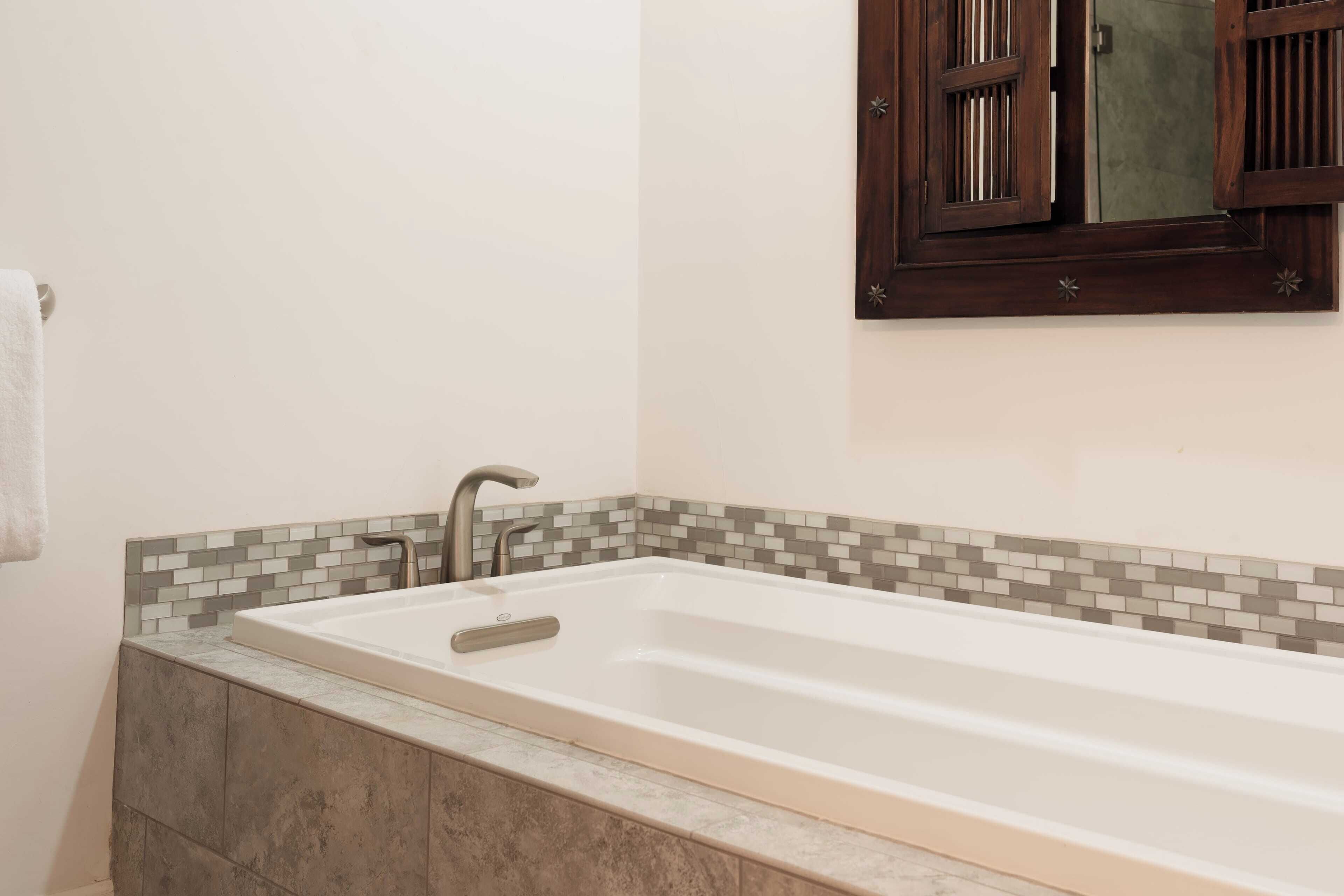 Une salle de bain avec une grande baignoire, un miroir et un mur recouvert de carreaux.