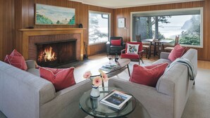 Una sala de estar con chimenea, un sofá, una mesa de centro de vidrio y vistas al océano.