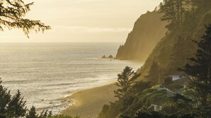 Un paisaje costero con playa, acantilados cubiertos de bosque y una casa.