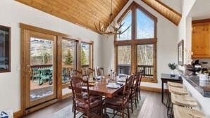 A dining area with a wooden table, chairs, and a chandelier. - Russell Home by Avantstay Expansive Deck, Stunning Views & Hot Tub! (Telluride)