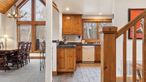 A spacious kitchen with wooden cabinets, a dining area with a large table and chairs, and a staircase with a wooden railing. - Russell Home by Avantstay Expansive Deck, Stunning Views & Hot Tub! (Telluride)