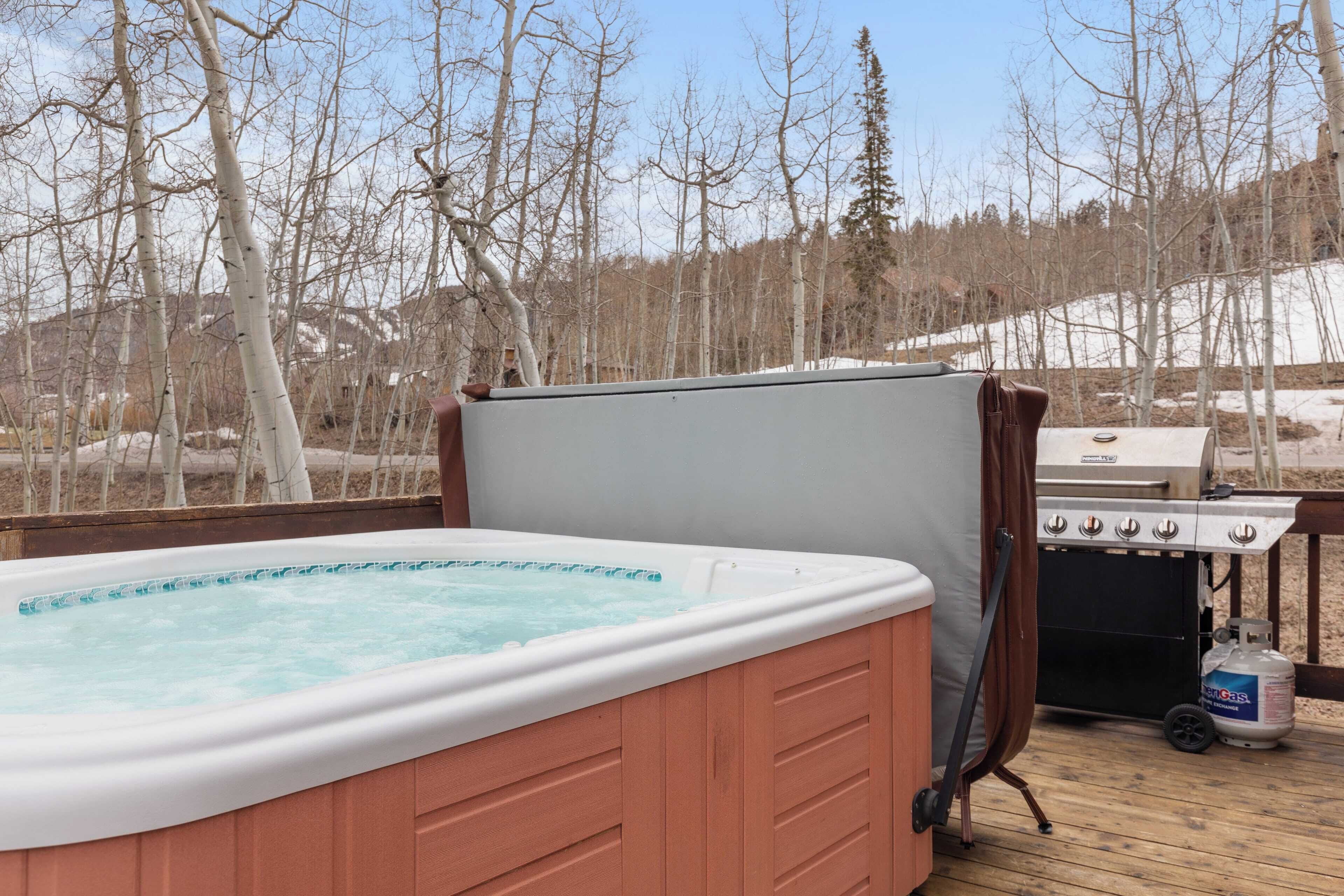 Un bain à remous sur une terrasse en bois, avec un barbecue et une bouteille de propane à proximité.