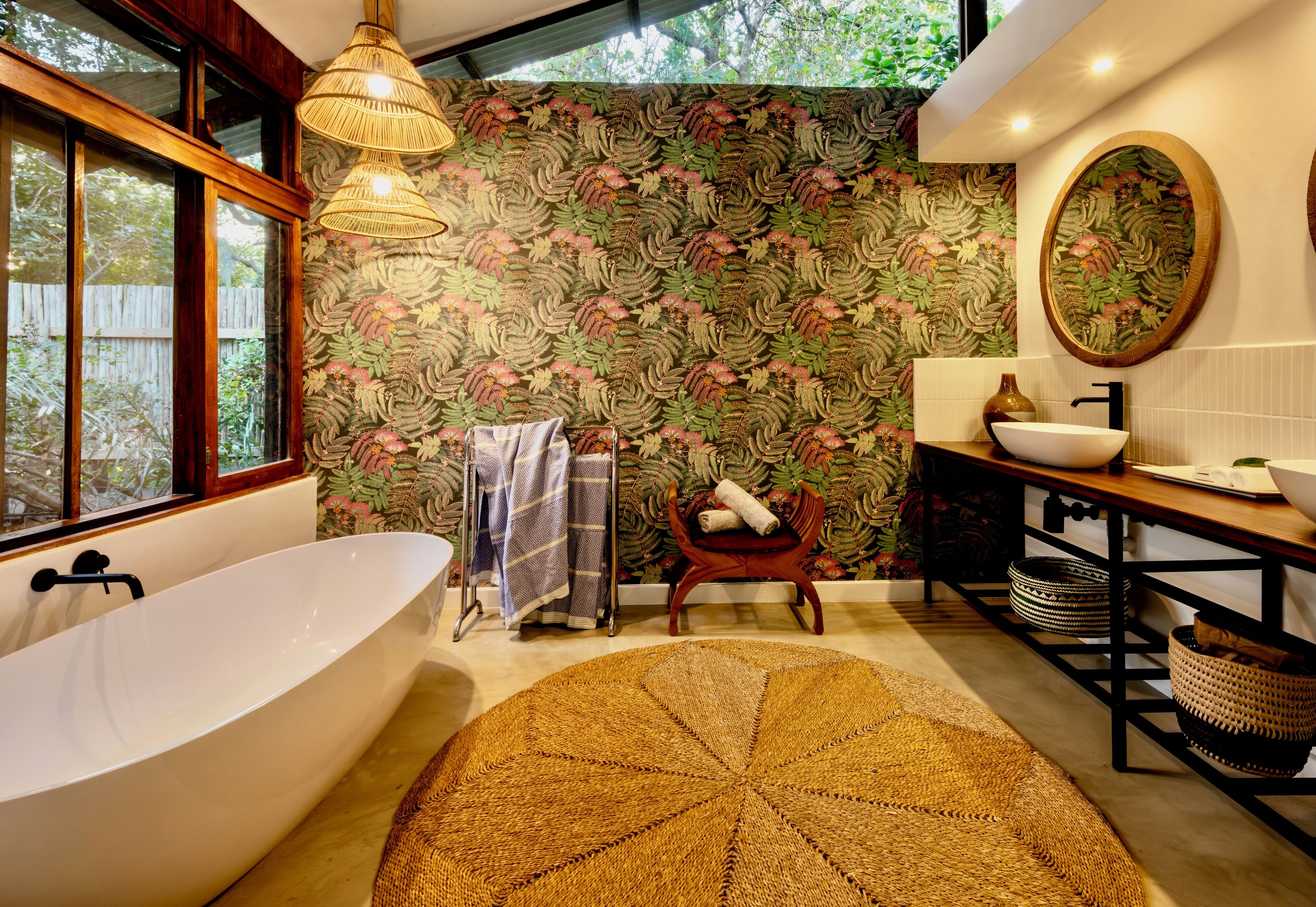 A modern bathroom with a freestanding bathtub, a round woven rug, and a large mirror above the sink.