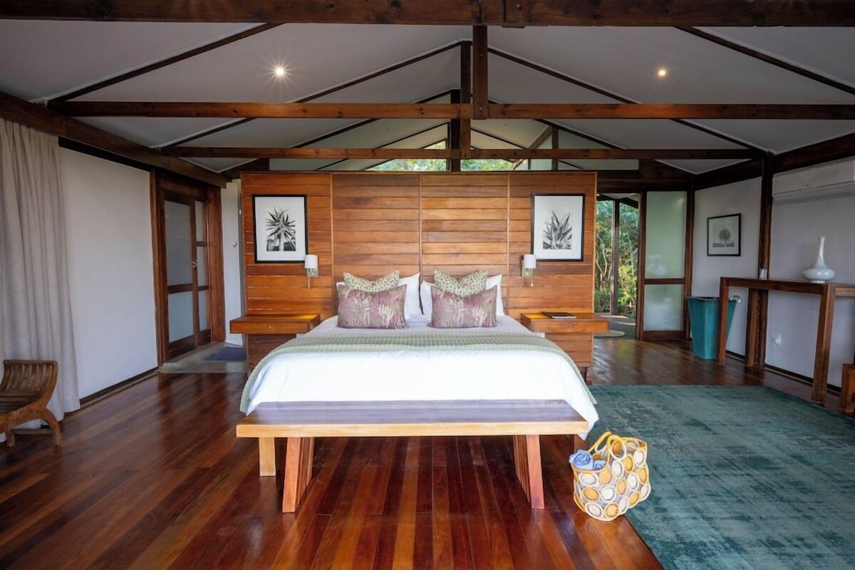 A spacious bedroom with a large bed, wooden headboard, and a view of the outdoors.